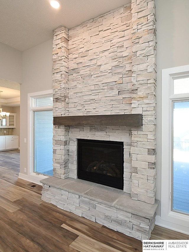 interior details featuring baseboards, visible vents, wood finished floors, a fireplace, and a notable chandelier