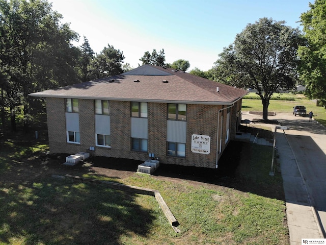 exterior space featuring brick siding, a yard, and roof with shingles