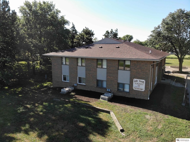 rear view of property featuring a yard, roof with shingles, and brick siding