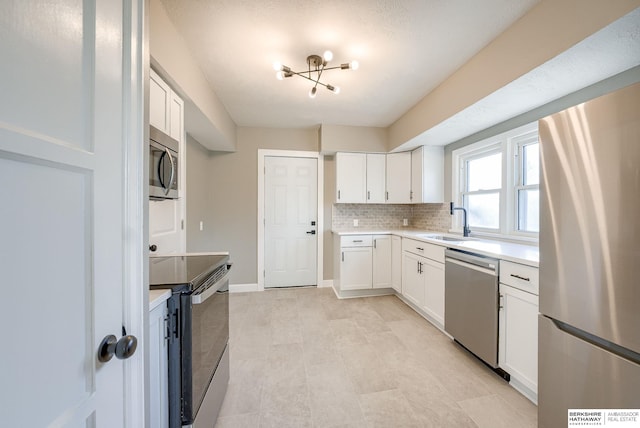 kitchen with stainless steel appliances, light countertops, backsplash, white cabinets, and a sink