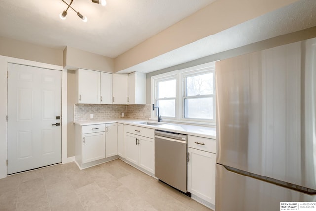 kitchen with a sink, white cabinetry, light countertops, stainless steel dishwasher, and freestanding refrigerator