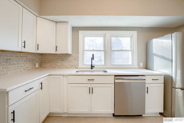 kitchen featuring decorative backsplash, white cabinets, freestanding refrigerator, stainless steel dishwasher, and a sink