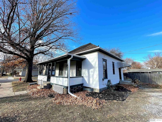 view of side of home with covered porch and fence