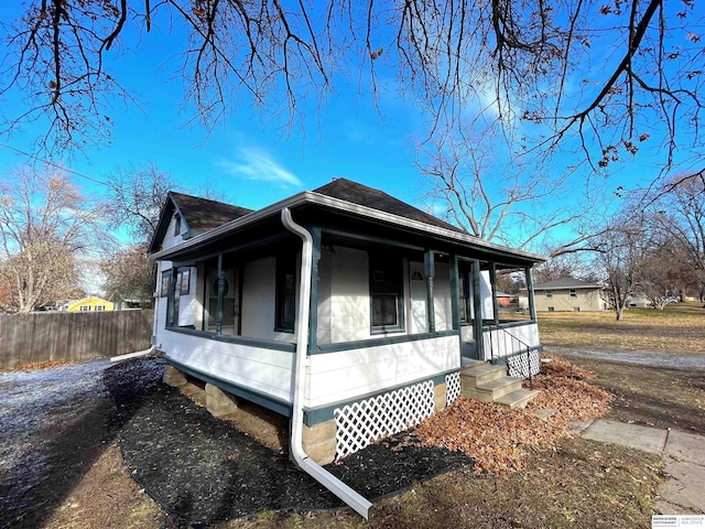 view of property exterior featuring a porch, roof with shingles, and fence