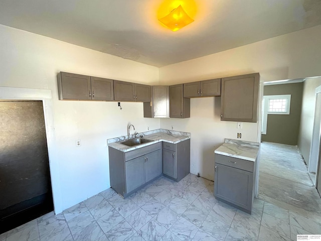 kitchen featuring gray cabinets, marble finish floor, light countertops, and a sink