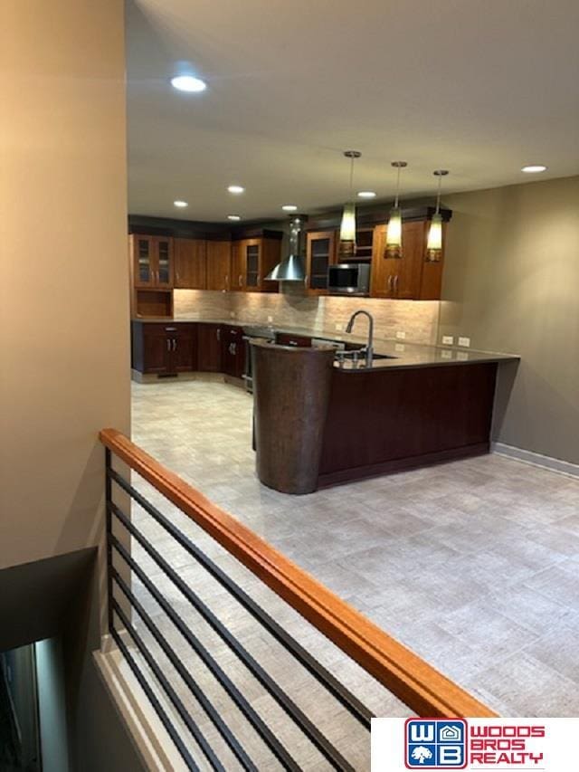 bar featuring a sink, hanging light fixtures, wall chimney range hood, tasteful backsplash, and stainless steel microwave