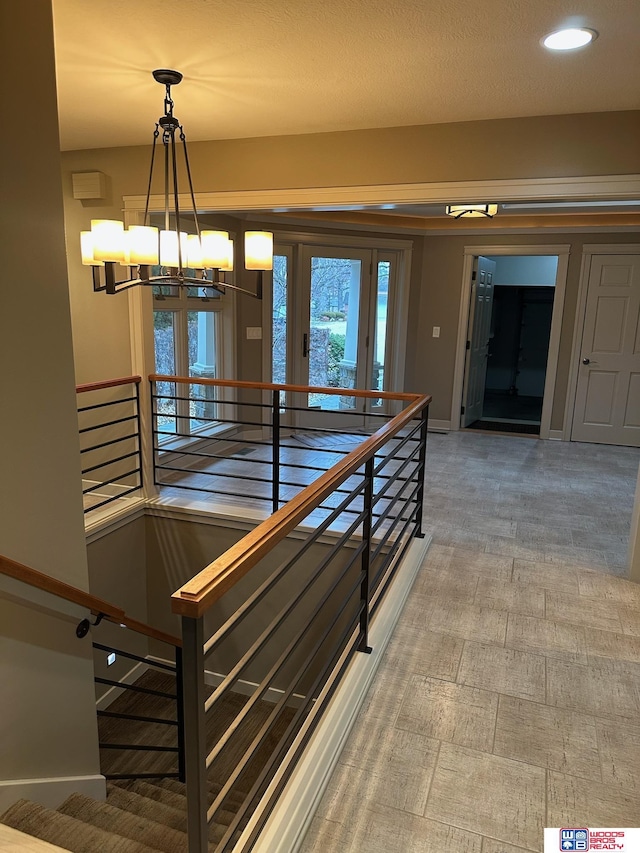 hall featuring an inviting chandelier, baseboards, and an upstairs landing