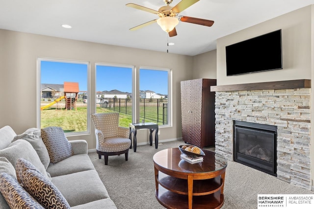 carpeted living room featuring a ceiling fan, recessed lighting, a stone fireplace, and baseboards