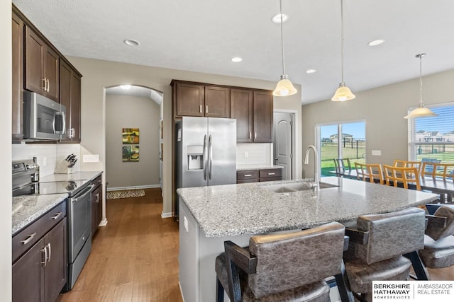 kitchen featuring arched walkways, stainless steel appliances, wood finished floors, a sink, and dark brown cabinets