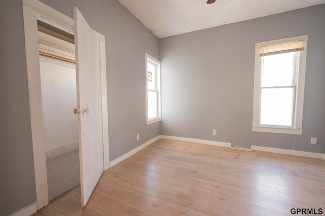 unfurnished bedroom featuring light wood-style floors, multiple windows, and baseboards