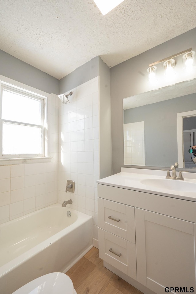 full bath with shower / bathtub combination, a textured ceiling, toilet, wood finished floors, and vanity