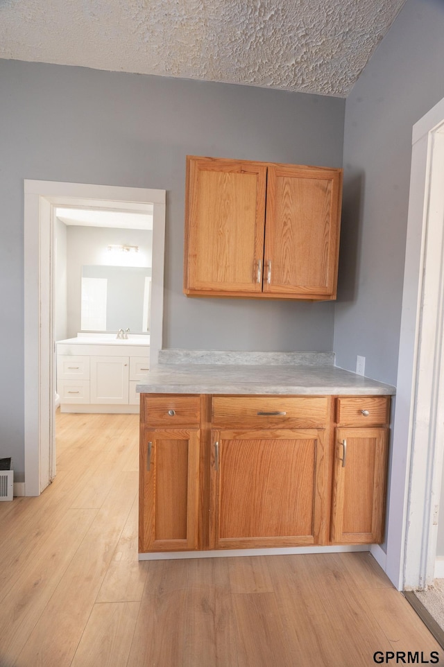 kitchen with light countertops, visible vents, light wood-style floors, brown cabinetry, and a textured ceiling