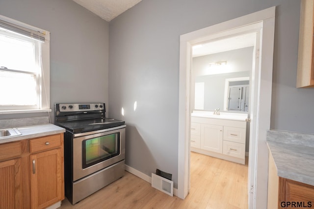 kitchen featuring light wood-type flooring, stainless steel electric range oven, visible vents, and light countertops