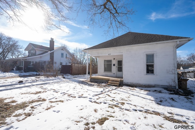 rear view of house featuring covered porch, roof with shingles, and fence