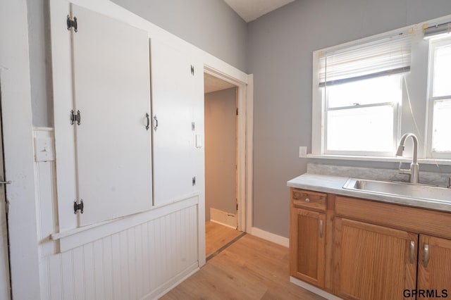 kitchen with a sink, baseboards, light countertops, light wood-type flooring, and brown cabinetry