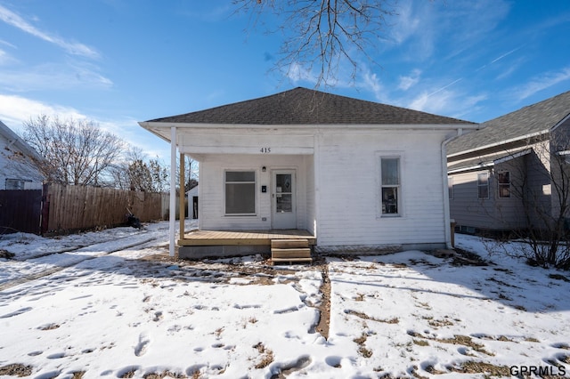 bungalow-style home with covered porch, a shingled roof, and fence