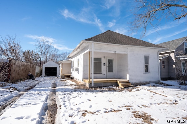 view of front of house with an outbuilding, roof with shingles, a detached garage, a porch, and fence