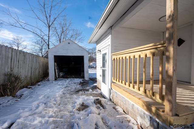 view of snowy exterior with an outbuilding, fence, a detached garage, and a storage unit