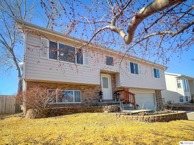 raised ranch featuring brick siding, an attached garage, a front lawn, and fence