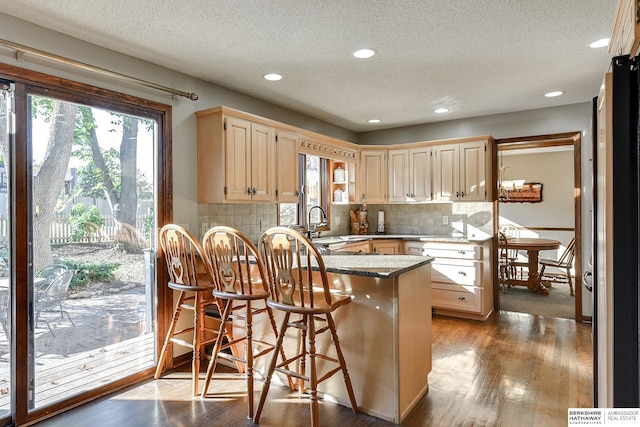 kitchen with a peninsula, dark wood-style flooring, a sink, backsplash, and a kitchen bar