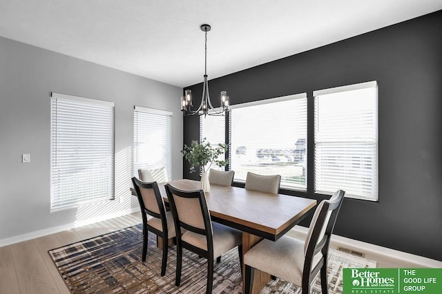 dining space featuring a healthy amount of sunlight, wood finished floors, visible vents, and a notable chandelier