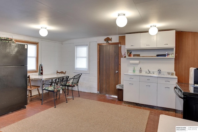 kitchen with white cabinets, light countertops, freestanding refrigerator, open shelves, and concrete block wall