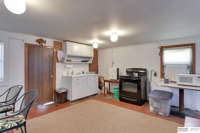 kitchen featuring white microwave, black range with electric stovetop, white cabinets, light countertops, and concrete block wall