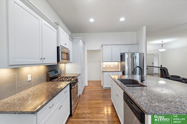 kitchen with tasteful backsplash, a kitchen island with sink, stainless steel appliances, light wood-style floors, and a sink