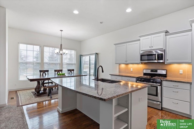 kitchen featuring a center island with sink, decorative backsplash, dark stone counters, stainless steel appliances, and a sink