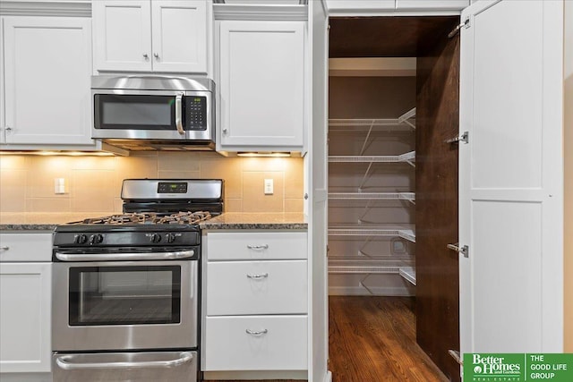 kitchen featuring stainless steel appliances, light stone countertops, white cabinetry, and tasteful backsplash