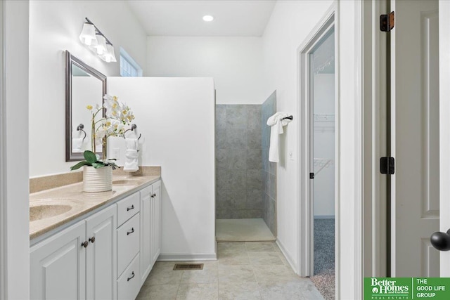 bathroom with double vanity, visible vents, tile patterned flooring, a walk in shower, and a sink