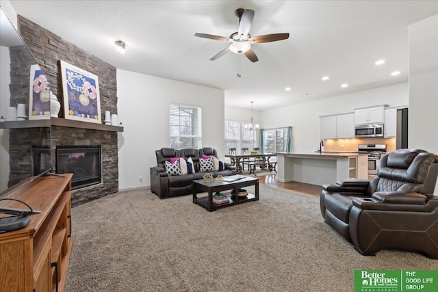 living room with recessed lighting, ceiling fan with notable chandelier, light colored carpet, and a stone fireplace