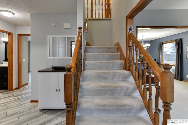 stairs with a textured ceiling, an inviting chandelier, wood finished floors, and baseboards