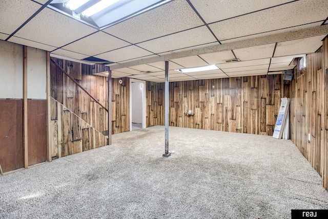 finished below grade area featuring carpet floors, a paneled ceiling, and wooden walls