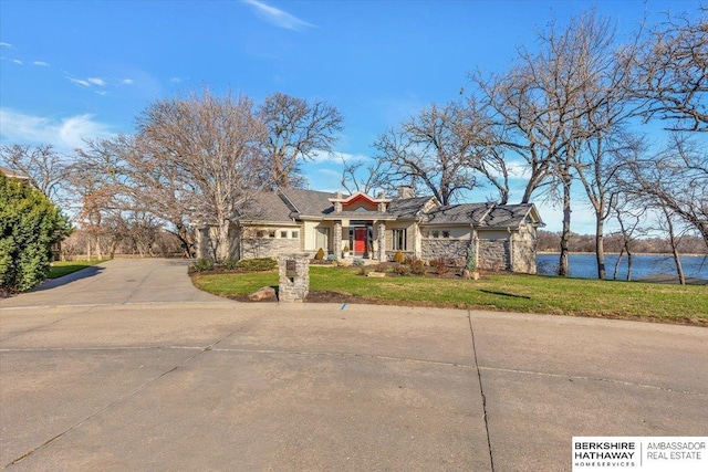 view of front of property with stone siding, a water view, driveway, and a front lawn