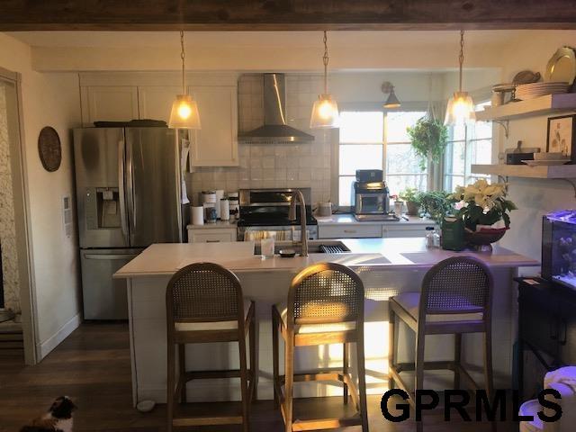 kitchen with white cabinets, stainless steel fridge with ice dispenser, wall chimney exhaust hood, stove, and light countertops