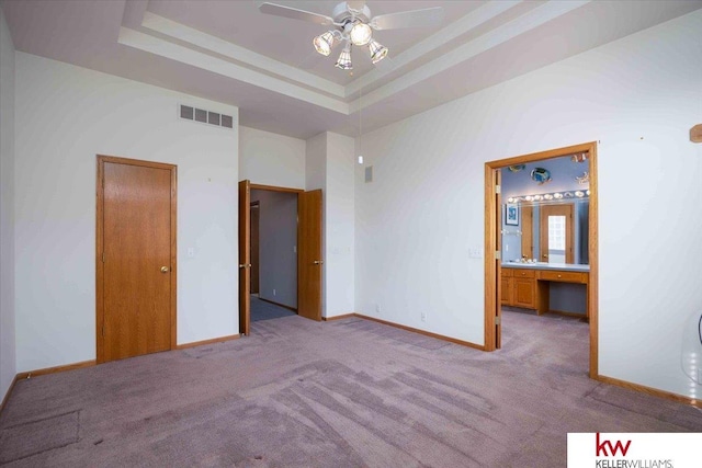 unfurnished bedroom with visible vents, a tray ceiling, ensuite bath, carpet, and baseboards