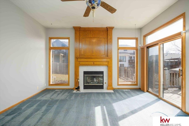 unfurnished living room featuring baseboards, a large fireplace, a ceiling fan, and carpet flooring