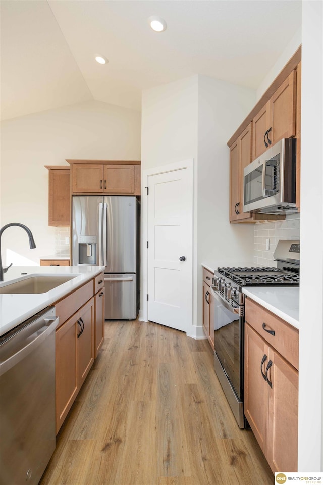 kitchen with stainless steel appliances, backsplash, light wood-style flooring, vaulted ceiling, and a sink