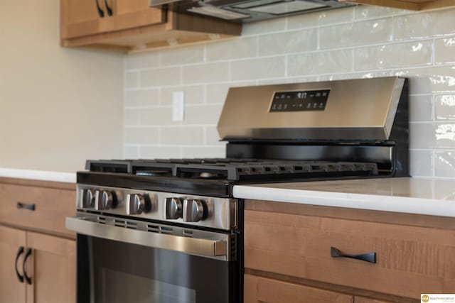 kitchen with brown cabinetry, decorative backsplash, stainless steel gas range, ventilation hood, and light countertops