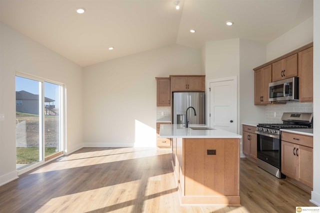 kitchen featuring light wood-style flooring, appliances with stainless steel finishes, vaulted ceiling, light countertops, and a sink