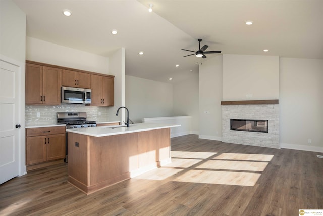 kitchen with a center island with sink, stainless steel appliances, open floor plan, a sink, and a stone fireplace