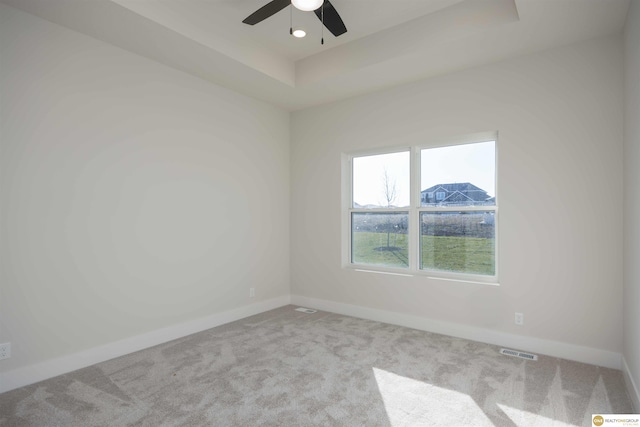 carpeted empty room with a raised ceiling, visible vents, ceiling fan, and baseboards