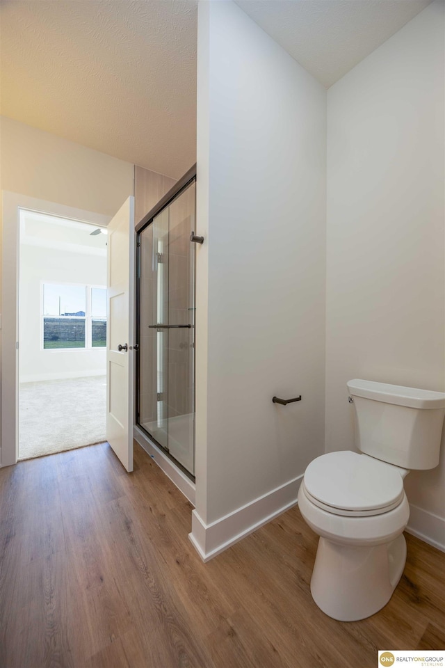 bathroom featuring a stall shower, toilet, and wood finished floors