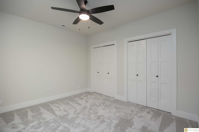 unfurnished bedroom featuring ceiling fan, visible vents, baseboards, multiple closets, and carpet