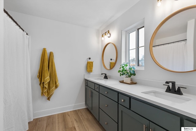 full bath featuring double vanity, wood finished floors, a sink, and baseboards