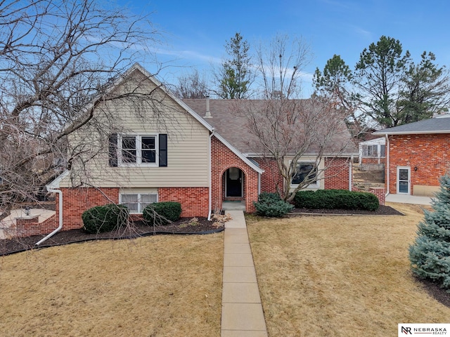 split level home with a shingled roof, a front yard, and brick siding