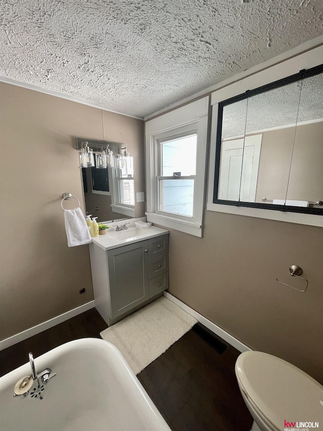 full bath featuring a textured ceiling, toilet, vanity, baseboards, and a freestanding bath