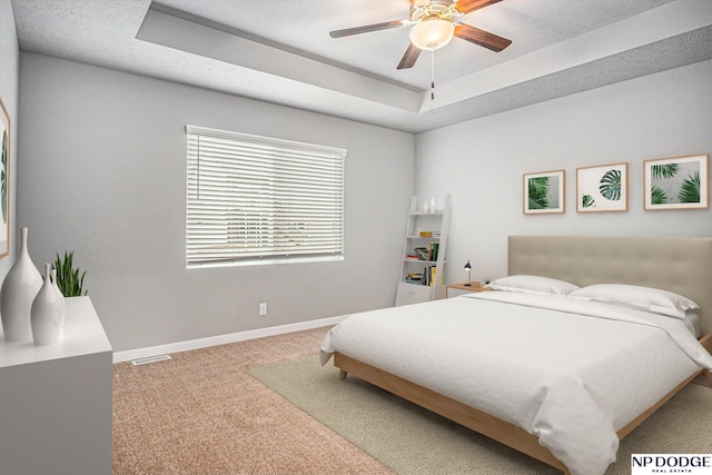 carpeted bedroom with baseboards, visible vents, a tray ceiling, and a ceiling fan