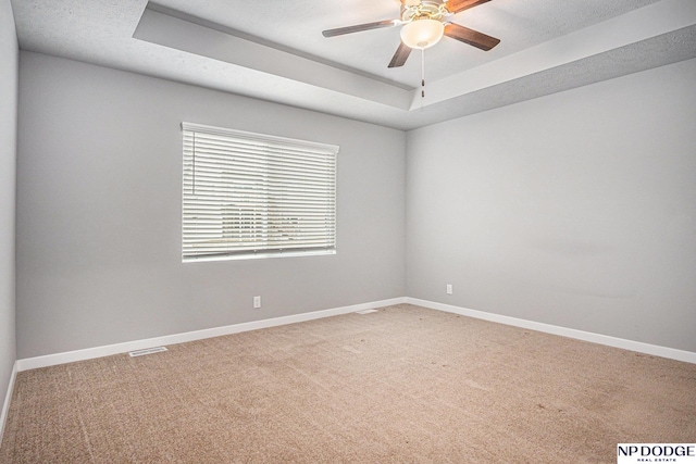 spare room with light colored carpet, visible vents, baseboards, a ceiling fan, and a raised ceiling